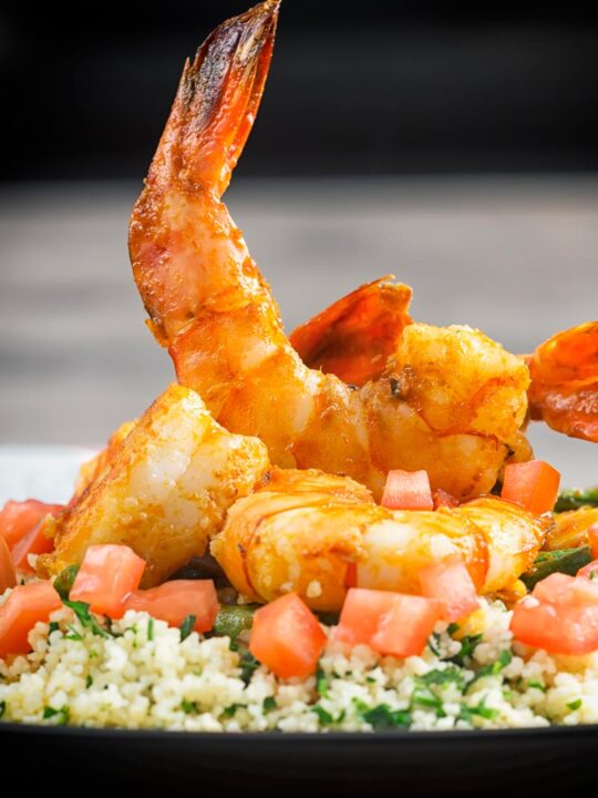 Portrait image of harissa garlic prawns served on a bed of buttered couscous