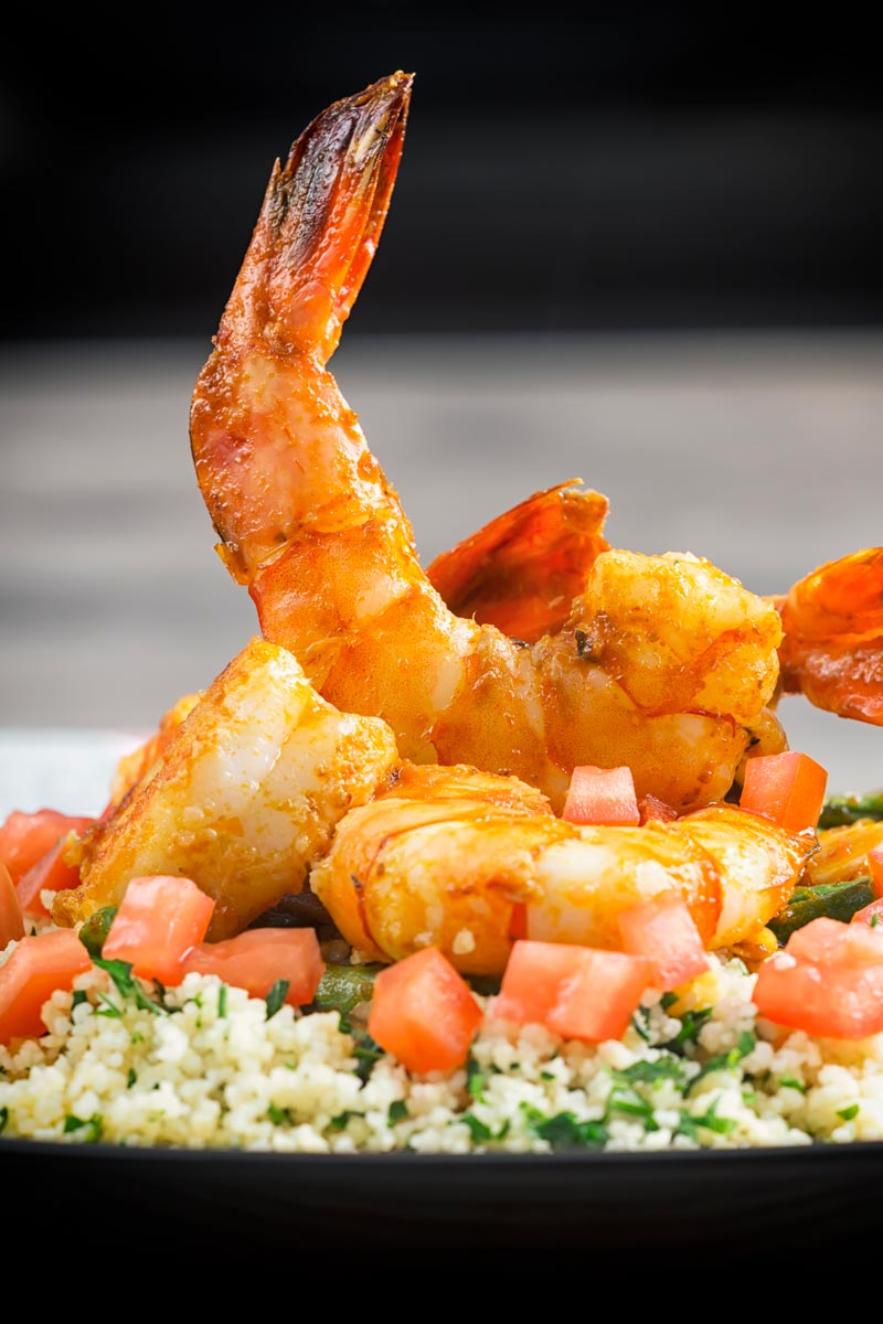 Portrait image of harissa garlic prawns served on a bed of buttered couscous