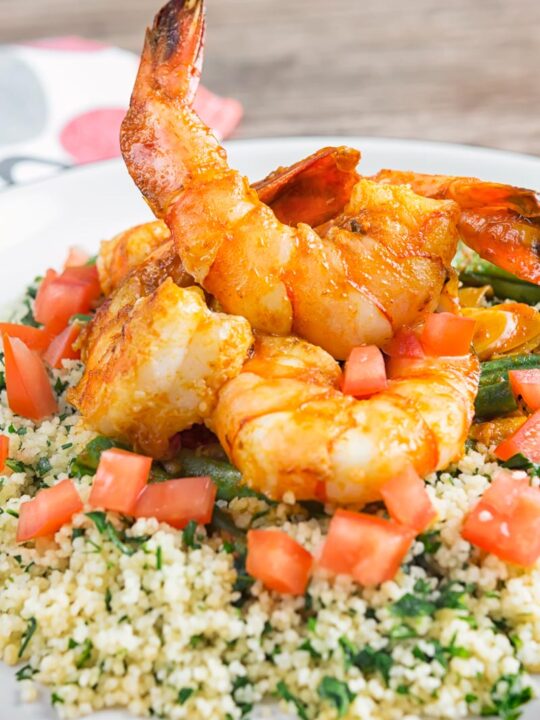 Portrait close up image of harissa garlic prawns served on a bed of buttered couscous served on a white plate