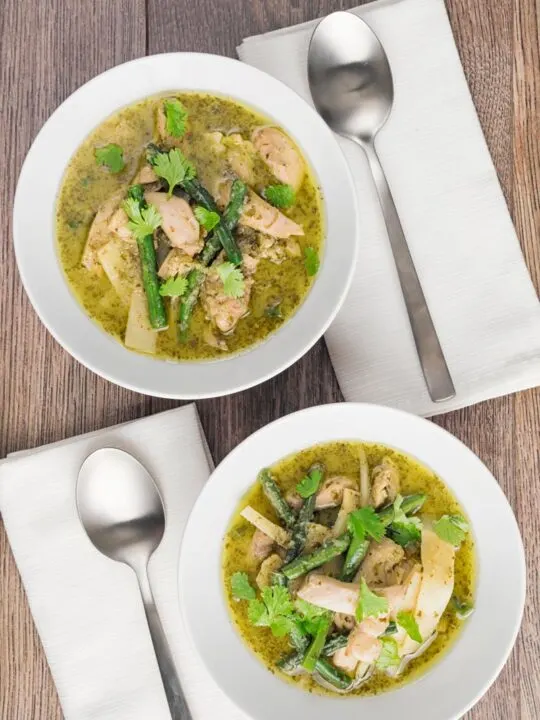 Portrait overhead image of Thai Green Chicken Curry featuring green beans and bamboo shoots served in two white bowls