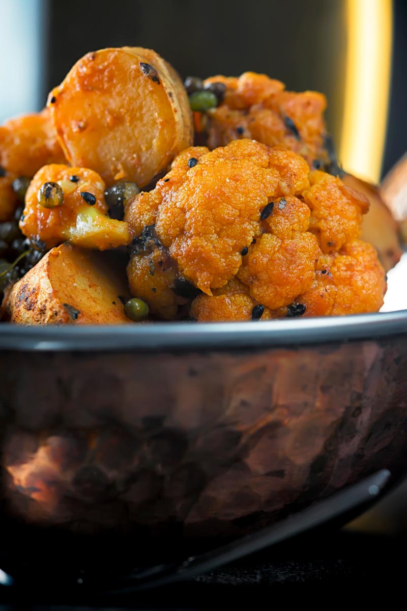 Portrait close up image of an aloo gobi Indian curry in a copper coloured curry bowl