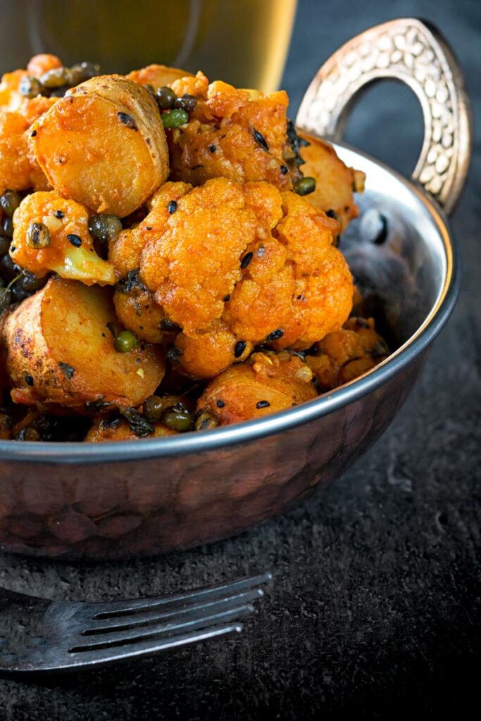 Portrait image of an aloo gobi Indian curry in a copper coloured curry bowl