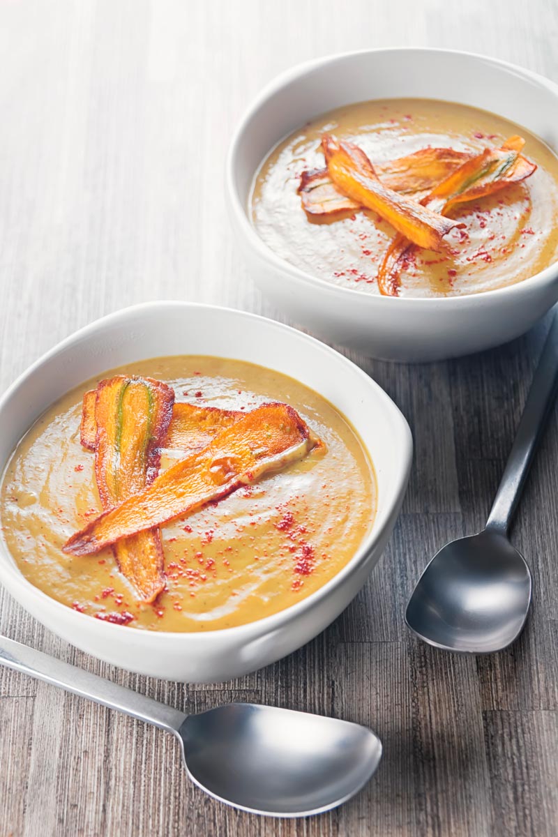 Portrait image of a creamy curried parsnip soup served in two bowls with fried carrot slices and paprika sprinkles