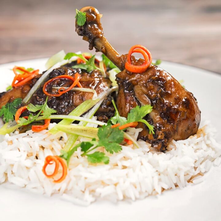 Square image of garlic and ginger chicken legs served on a bed of white rice with julienned chilli and spring onions