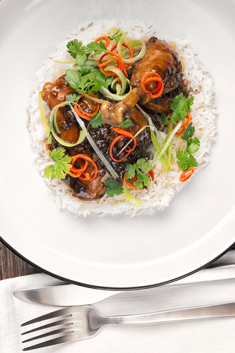 Portrait overhead image of garlic and ginger chicken legs served on a bed of white rice with julliened chilli and spring onions