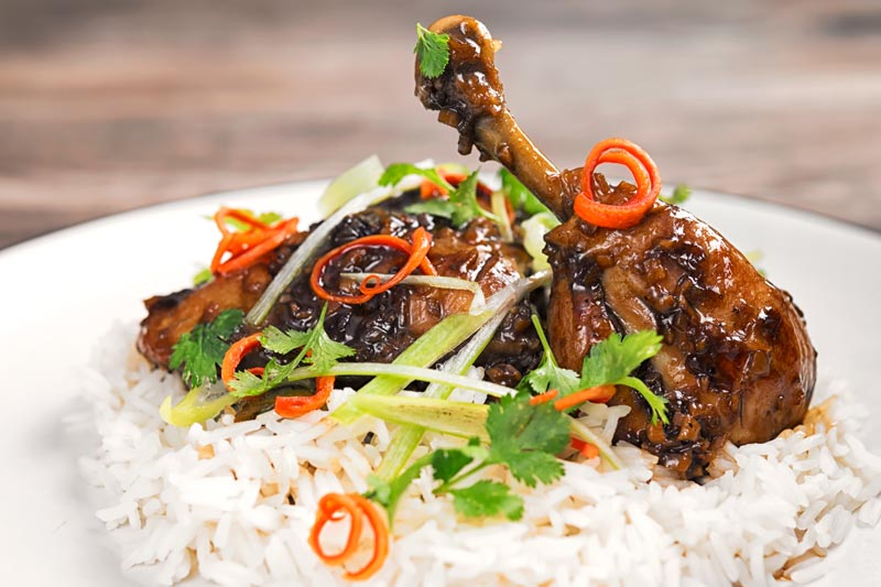 Landscape image of garlic and ginger chicken legs served on a bed of white rice with julienned chilli and spring onions