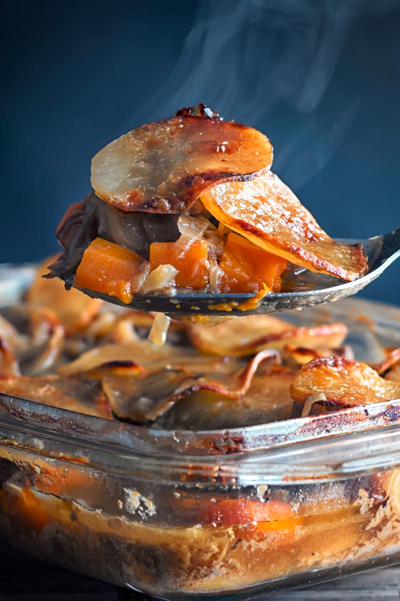 Portrait image of a steaming portion of lamb hot pot being taken from a pie featuring sliced potatoes and carrots