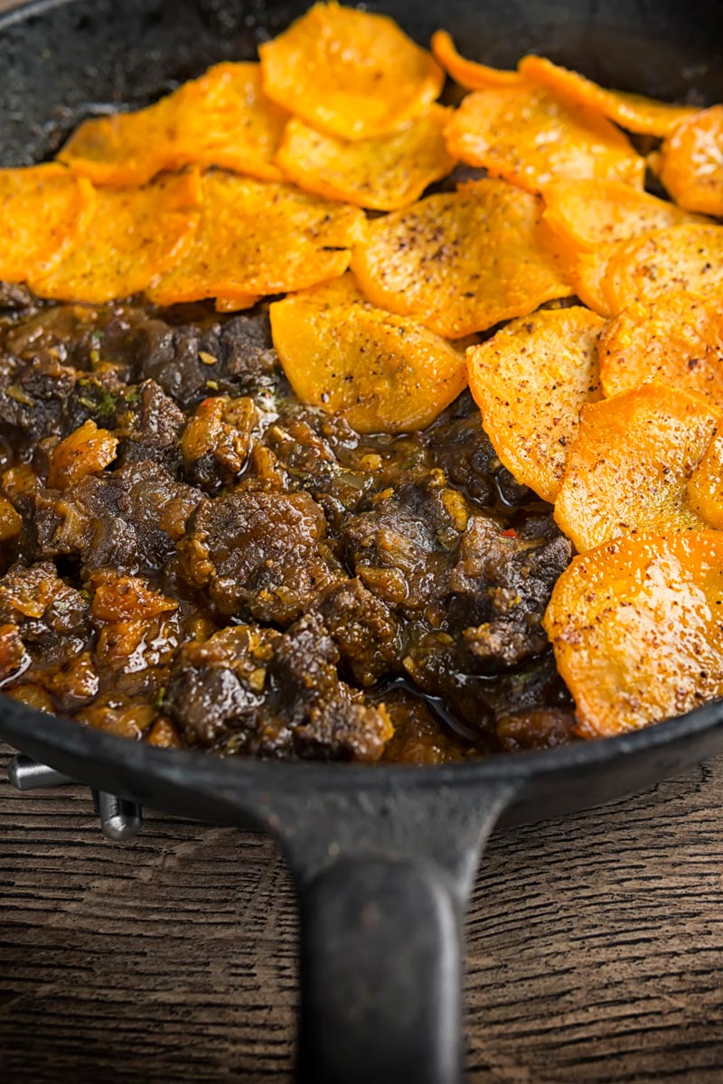 Portrait image of a beef hotpot served in a cast iron skillet with a sliced sweet potato topping