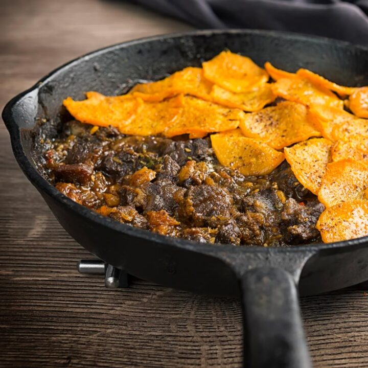 Square image of a beef hotpot served in a cast iron skillet with a sliced sweet potato topping