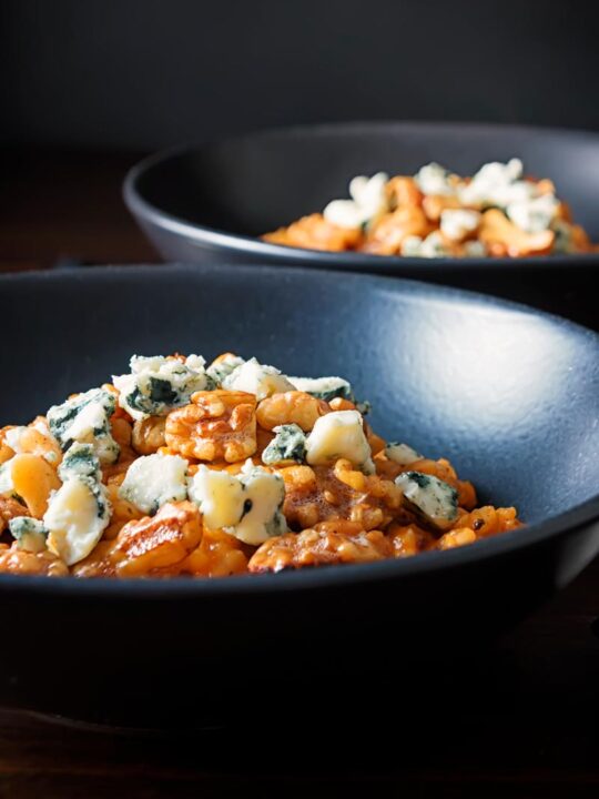 Portrait image of a pureed pumpkin risotto with blue cheese and walnuts served in two black bowls