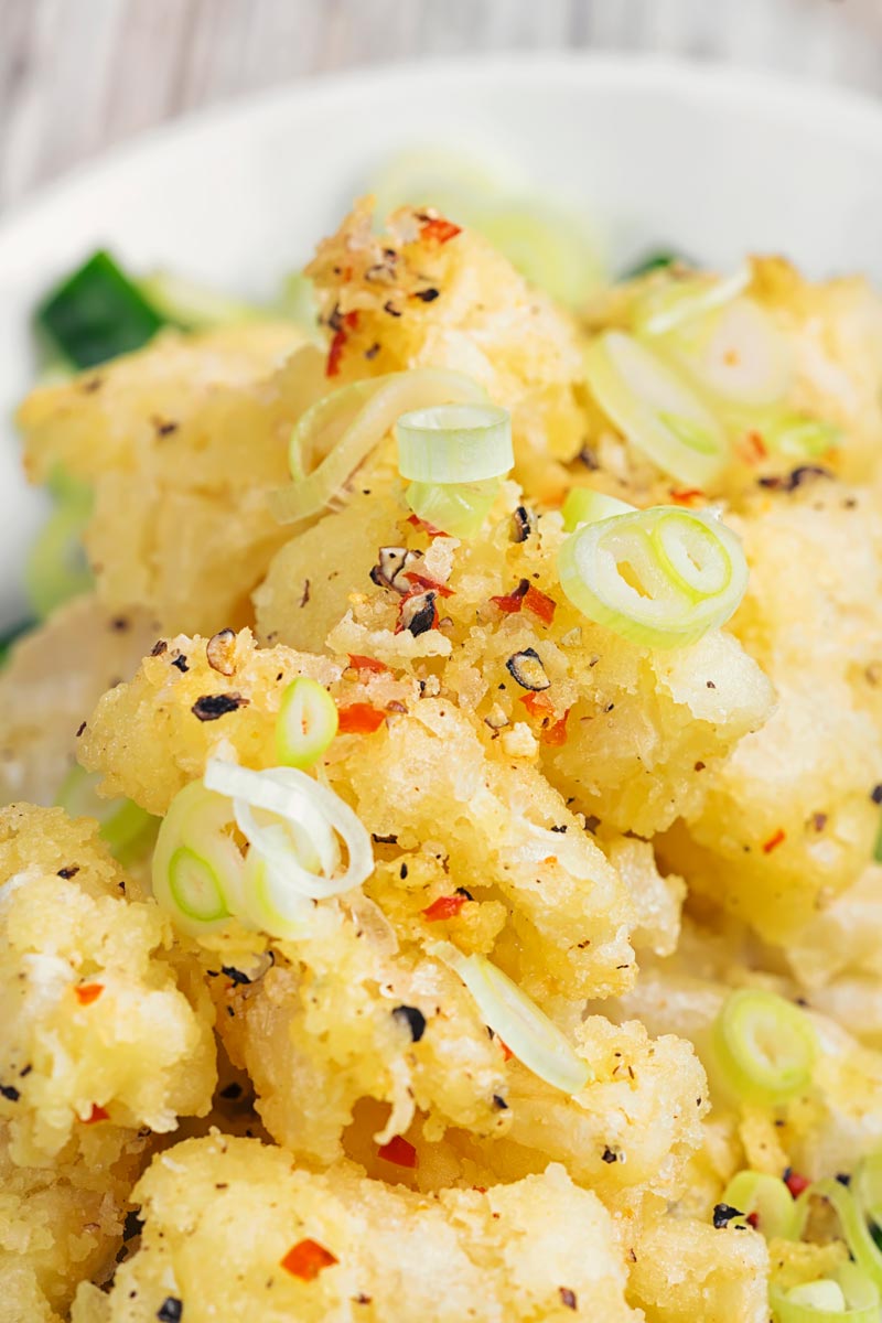 Portrait close up image of crispy salt and pepper squid served on pickled cucumber and a wedge of lemon served in a shallow white bowl