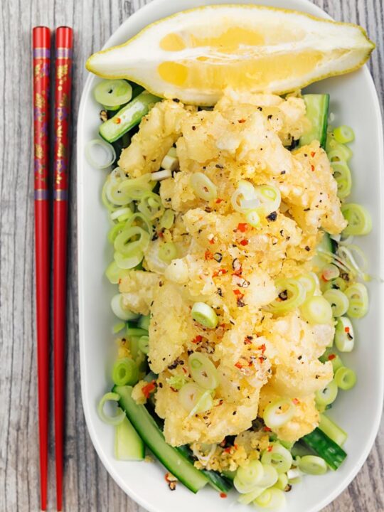 Portrait overhead image of crispy salt and pepper squid served on pickled cucumber, sliced spring onions and a wedge of lemon served in a shallow white bowl