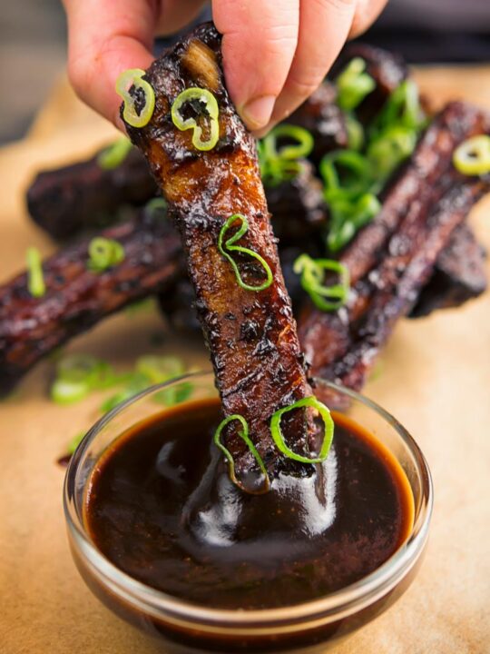 Portrait image of sticky Instant Pot Chinese spare ribs being dipped into a sauce