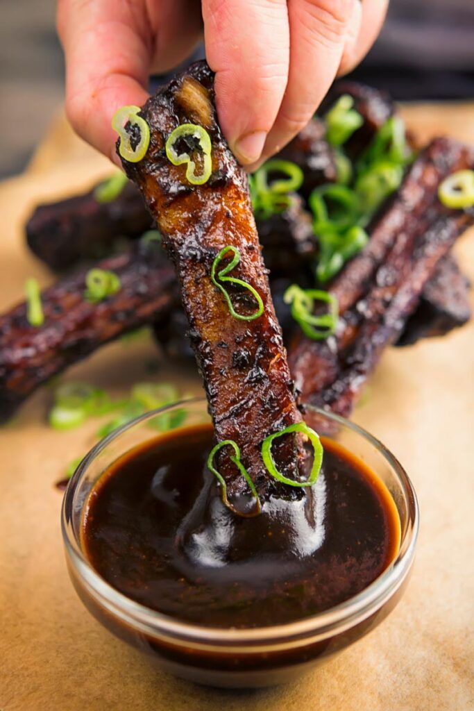 Portrait image of sticky Instant Pot Chinese spare ribs being dipped into a sauce