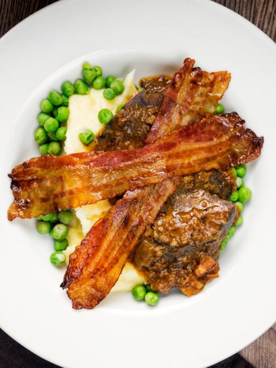 Portrait overhead image of bacon liver an onions with mash and peas served in a white bowl