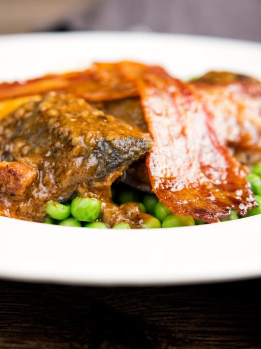 Portrait close up image of bacon liver an onions with mash and peas served in a white bowl