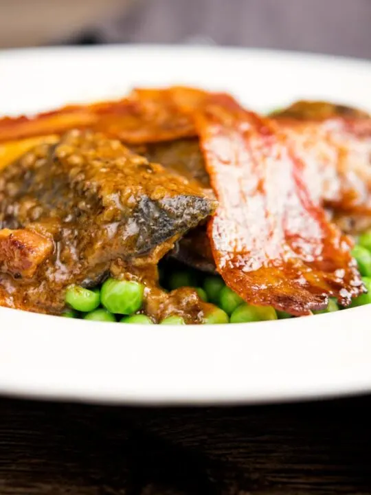 Portrait close up image of bacon liver an onions with mash and peas served in a white bowl