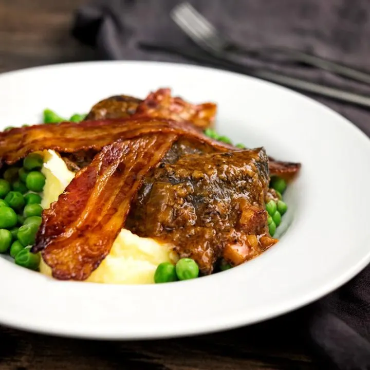 Square image of bacon liver an onions with mash and peas served in a white bowl