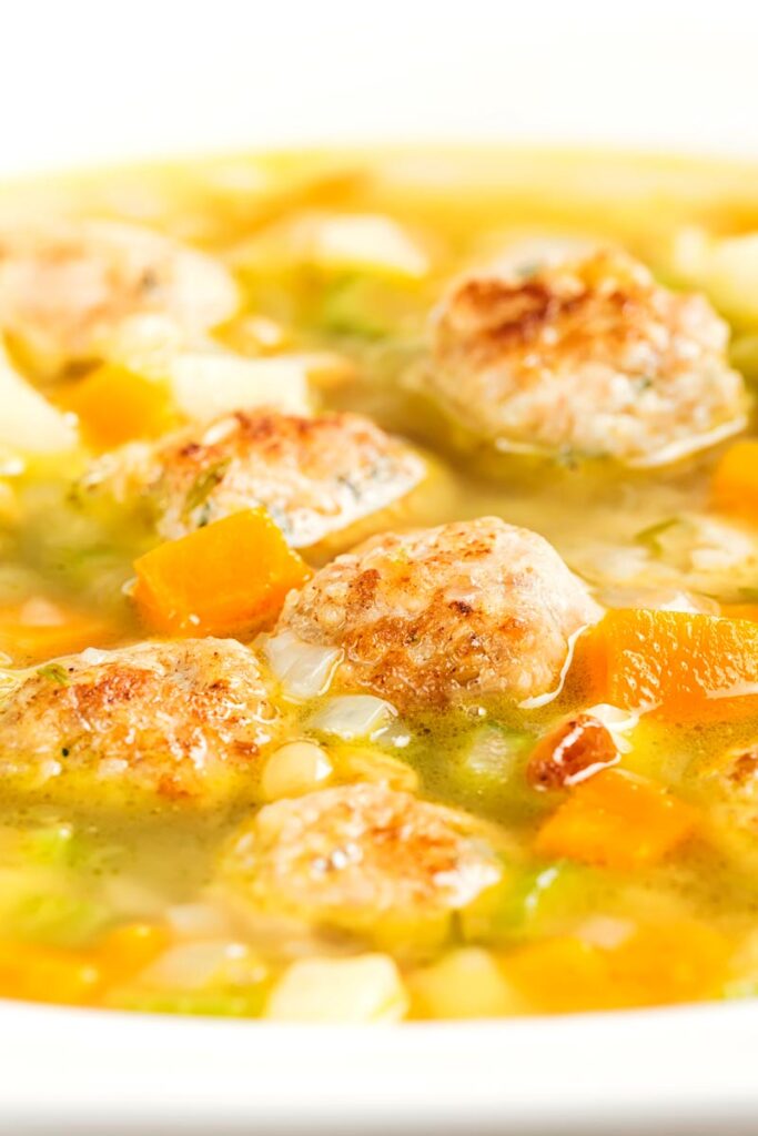 Portrait close up image of a simple meatball soup with diced vegetables and pork meatballs and a light broth in a white bowl