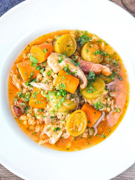 Portrait overhead image of a shredded rabbit stew with pearl barley, carrots and leeks served in a white bowl
