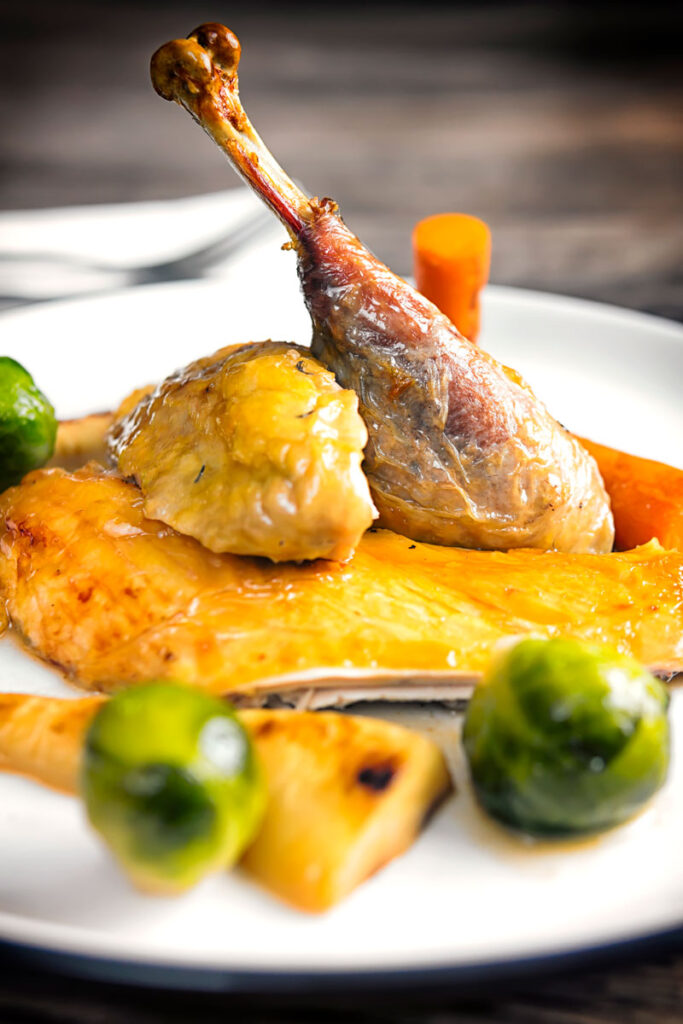 Close up portrait image of a guinea fowl leg served on a white plate with out of focus vegetables