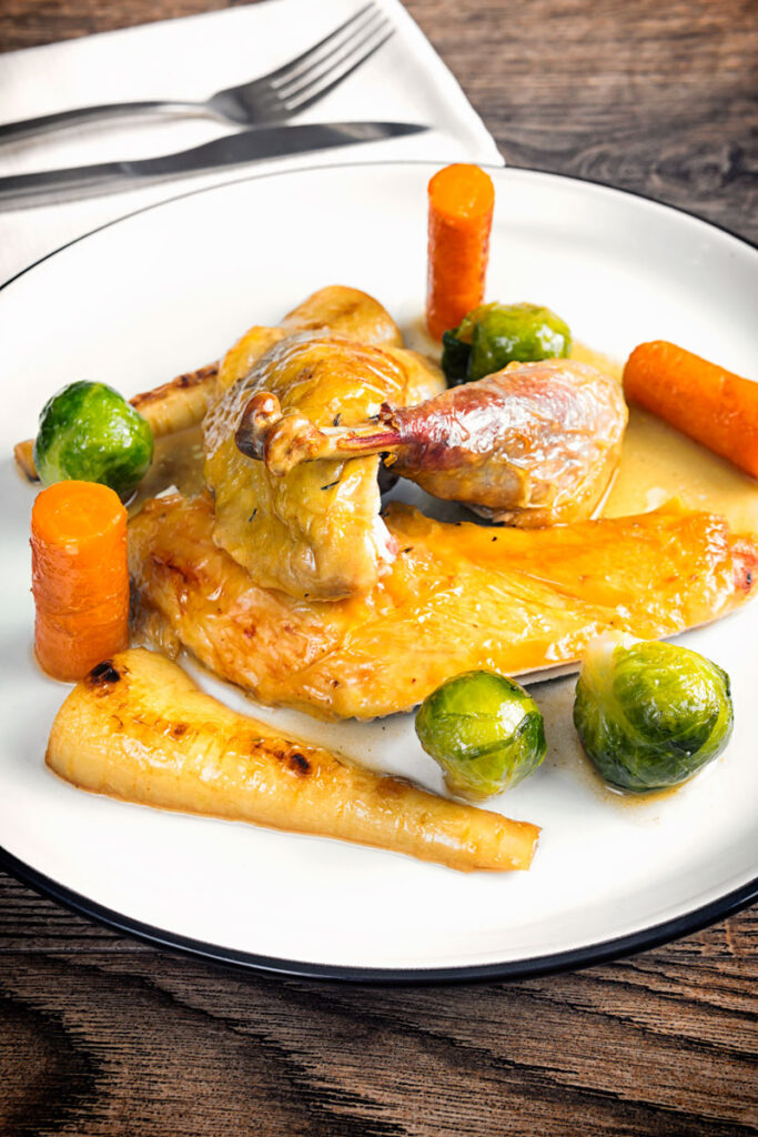 Portrait image of a guinea fowl leg served on a white plate with out of focus vegetables