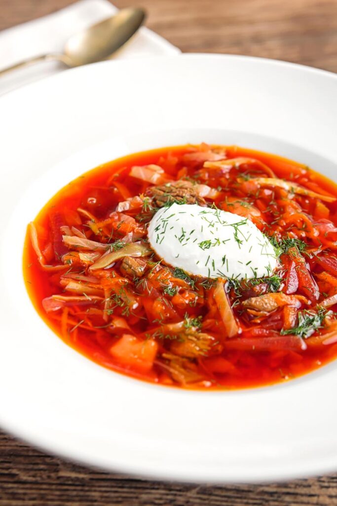 Portrait image of a Russian Borscht Soup served in a white bowl with sour cream and dill
