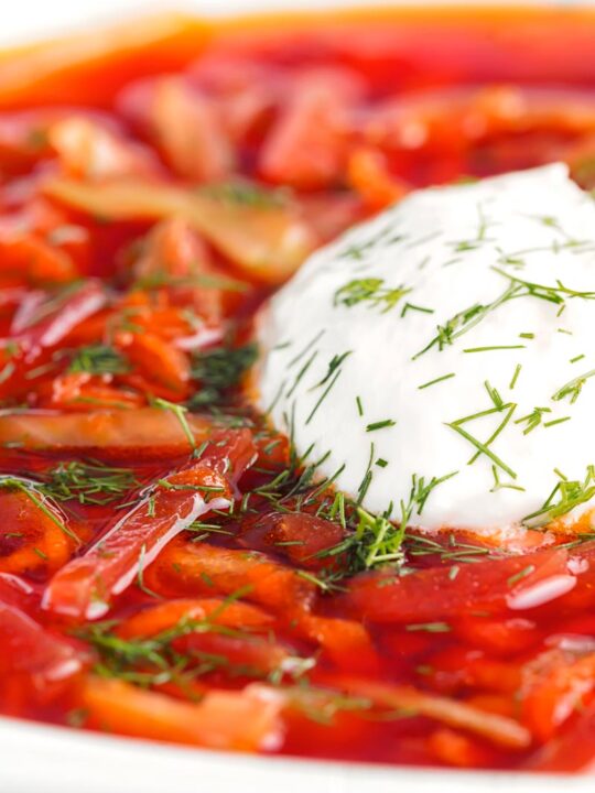 Portrait close up image of a Russian Borscht Soup served in a white bowl with sour cream and dill