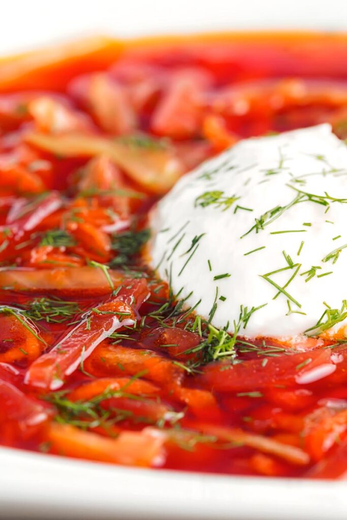 Portrait close up image of a Russian Borscht Soup served in a white bowl with sour cream and dill