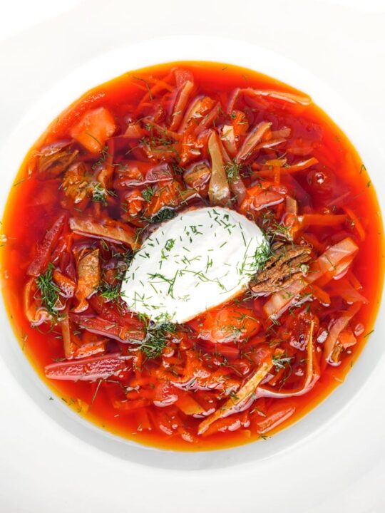 Portrait overhead image of a Russian Borscht Soup served in a white bowl with sour cream and dill