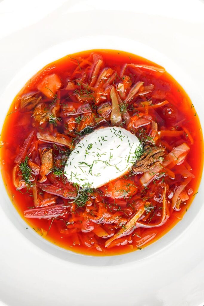 Portrait overhead image of a Russian Borscht Soup served in a white bowl with sour cream and dill
