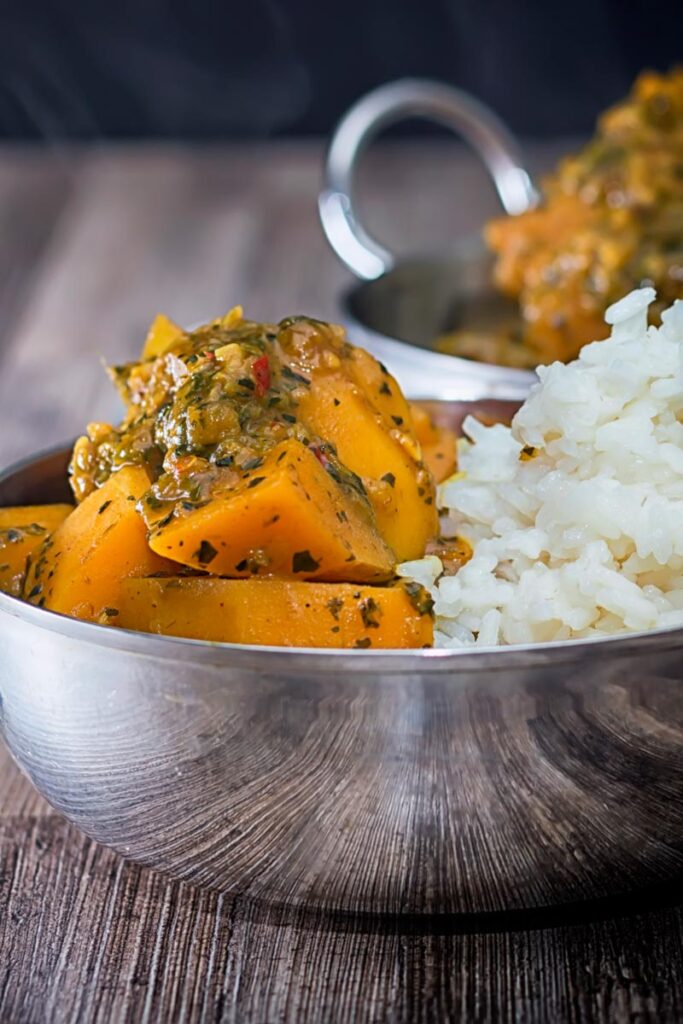 Portrait image of a steaming hot pumpkin curry with white rice served in a stainless steel curry bowl