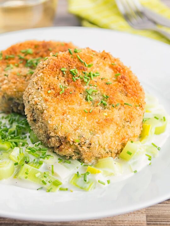 Portrait image of fish cakes served with leeks served on a white plate.