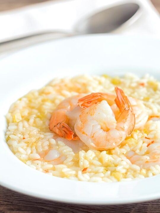 Portrait image of a lemon and chilli prawn risotto featuring 3 shrimp with tails on served in a white bowl
