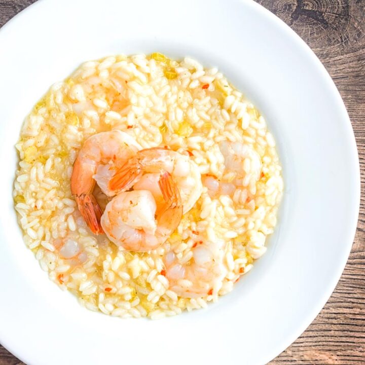 Square overhead image of a lemon and chilli prawn risotto featuring 3 shrimp with tails on served in a white bowl