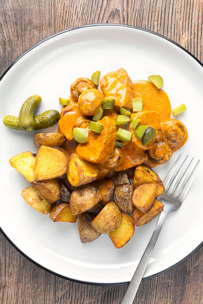 Portrait overhead image of a mushroom and pork stroganoff served with fried potatoes on a white plate with a chopped cournichon garnish