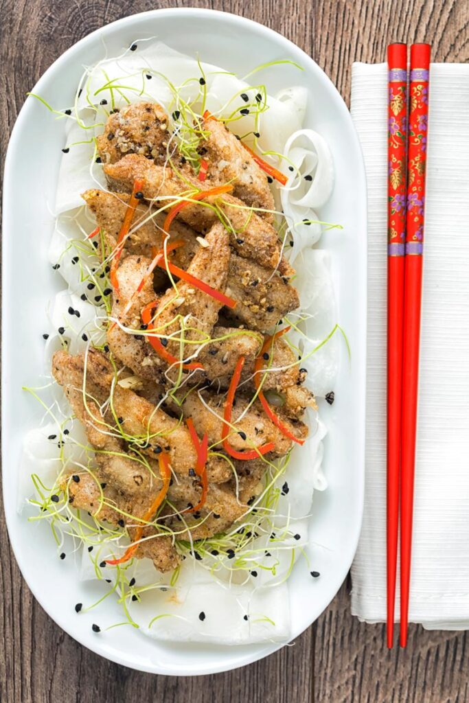 Overhead portrait image of salt and pepper chicken with pickled daikon and sprouted onion seeds with red chopsticks