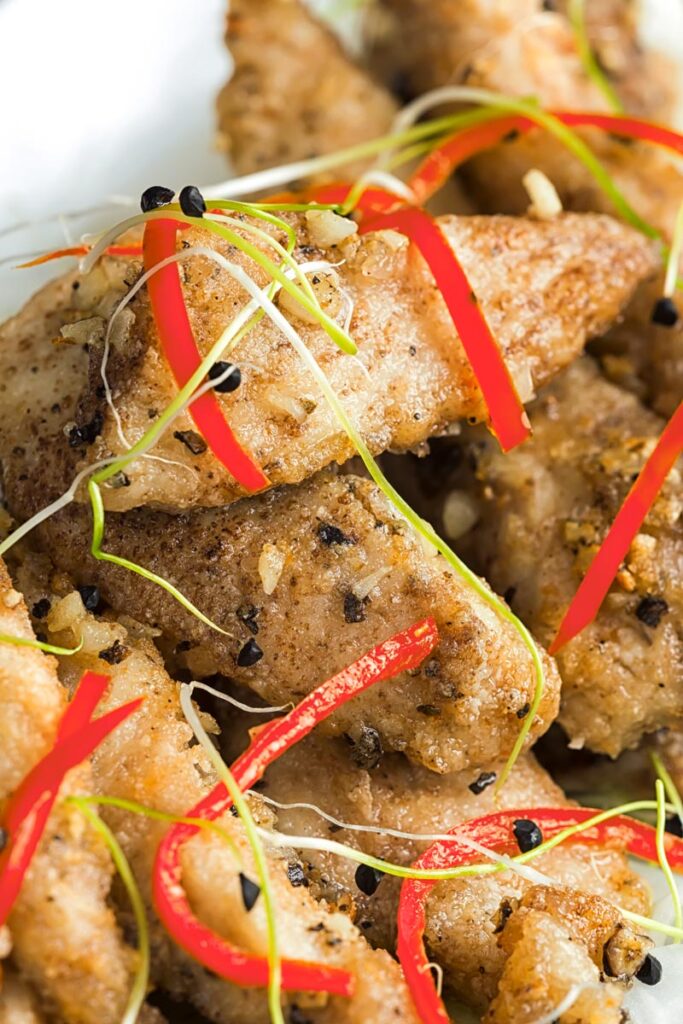 Portrait close up image of salt and pepper chicken with pickled daikon and sprouted onion seeds with red chopsticks