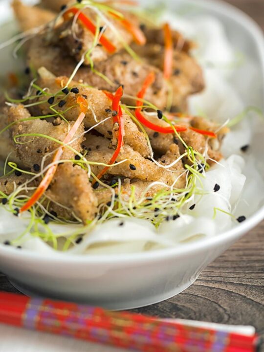 Portrait image of salt and pepper chicken with pickled daikon and sprouted onion seeds with red chopsticks