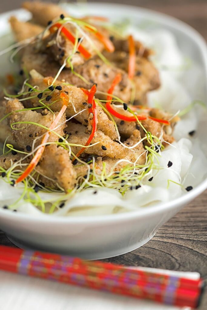 Portrait image of salt and pepper chicken with pickled daikon and sprouted onion seeds with red chopsticks