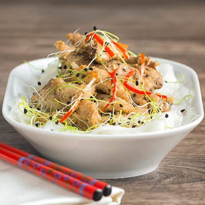 Square image of salt and pepper chicken with pickled daikon and sprouted onion seeds with red chopsticks