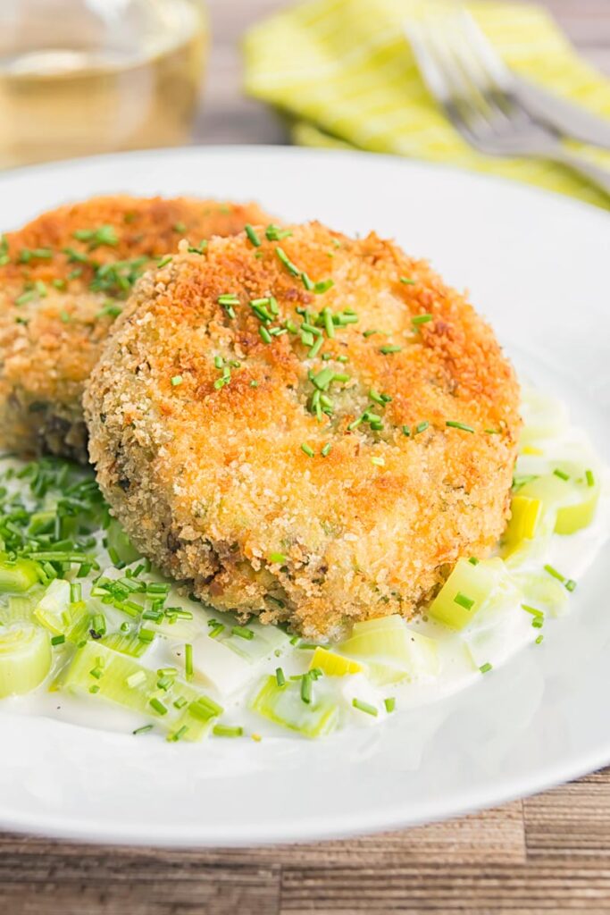 Portrait image of golden sardine and salmon fishcakes served on creamed leaks on a white plate