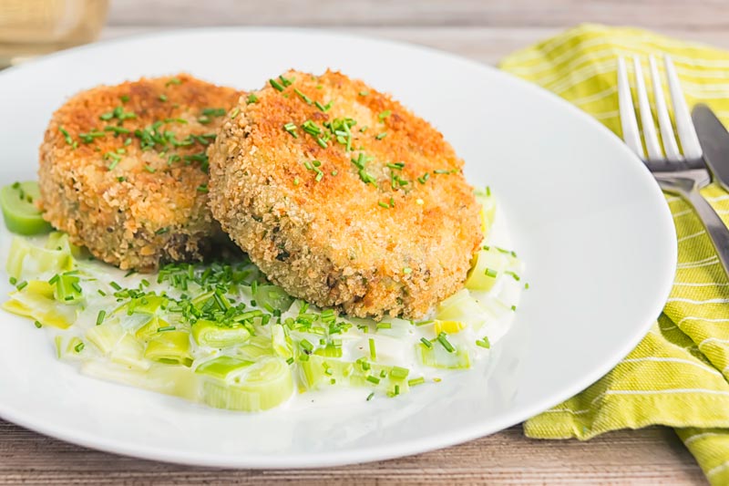 Landscape image of golden sardine and salmon fishcakes served on creamed leeks