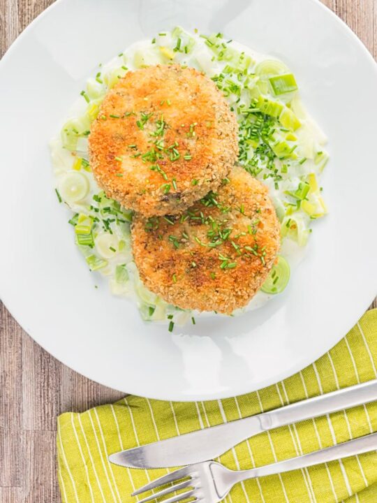 Portrait overhead image of golden sardine and salmon fishcakes served on creamed leeks