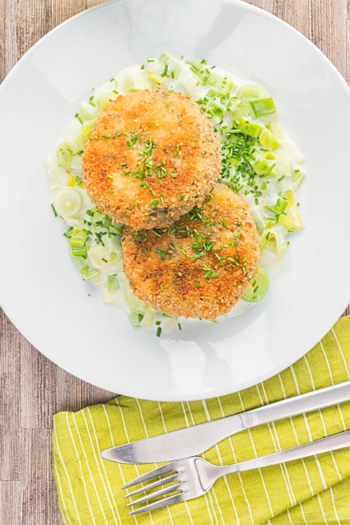 Portrait overhead image of golden sardine and salmon fishcakes served on creamed leeks