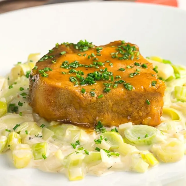 Square image of a portion of slow cooker pork loin that has been sliced served with creamed leeks on a white plate