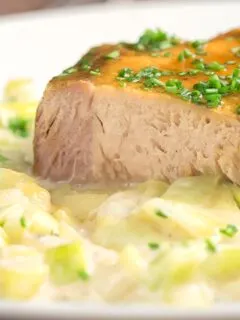 Portrait close up image of a portion of slow cooker pork loin that has been sliced served with creamed leeks on a white plate