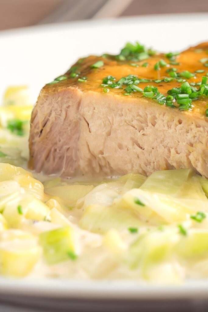 Portrait close up image of a portion of slow cooker pork loin that has been sliced served with creamed leeks on a white plate