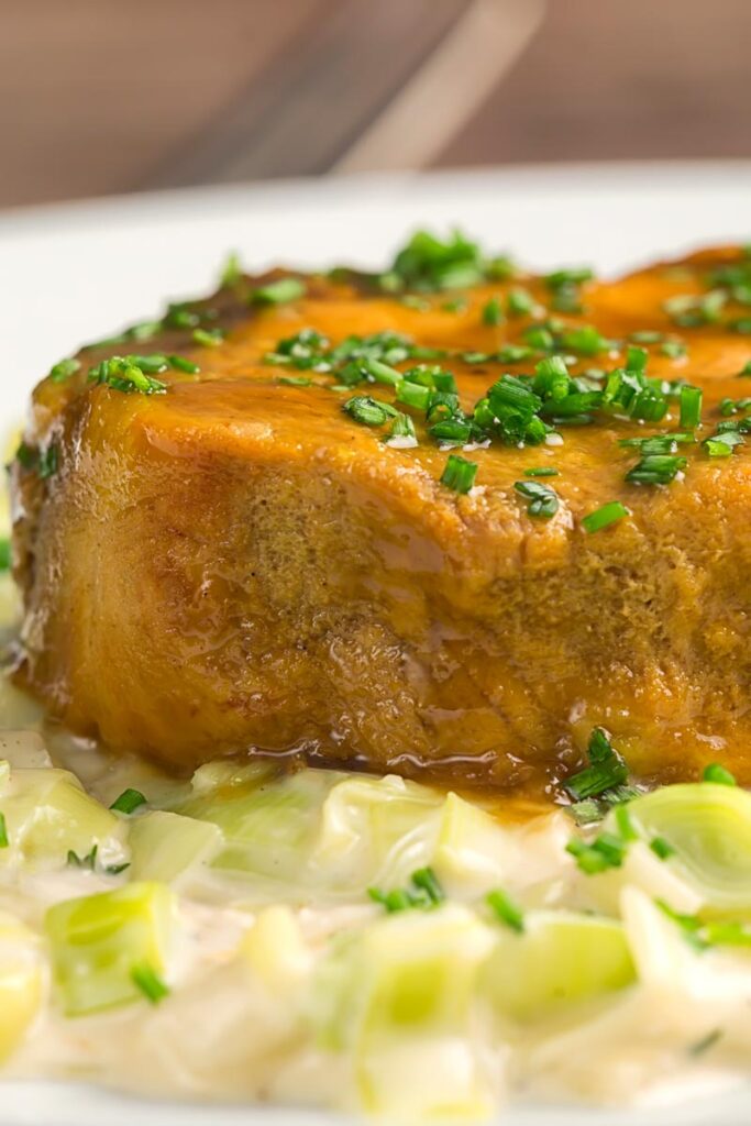 Portrait close up image of a portion of slow cooker pork loin served with creamed leeks on a white plate