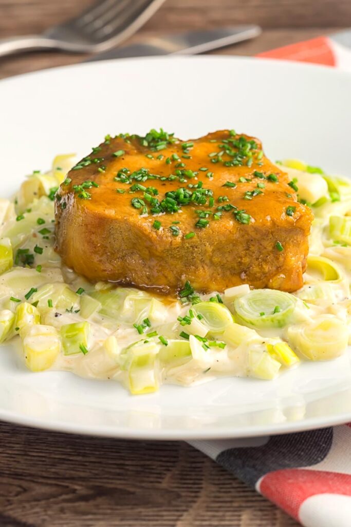 Portrait image of a portion of slow cooker pork loin served with creamed leeks on a white plate